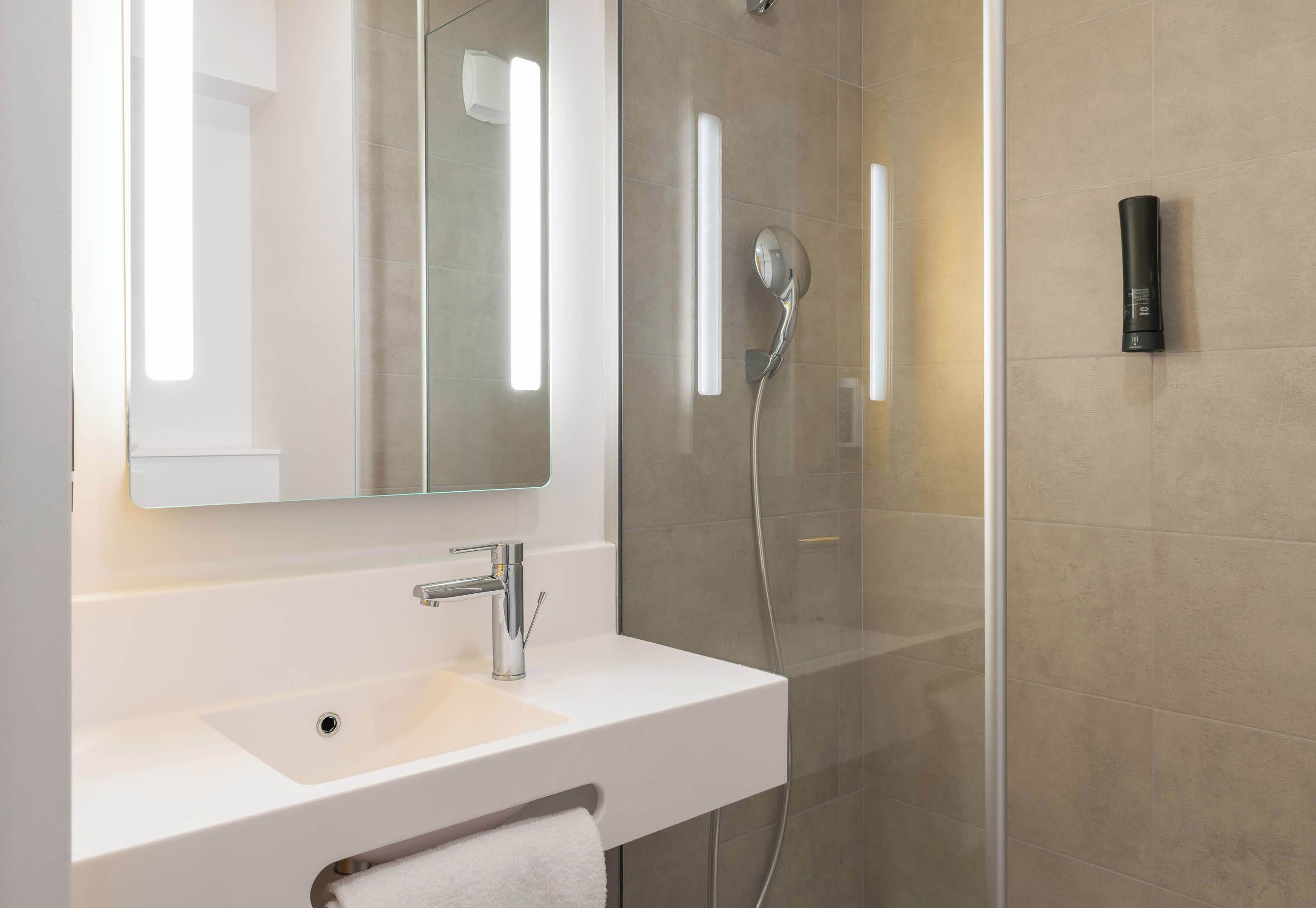 Un baño moderno con un lavamanos blanco, un espejo y una zona de ducha con mampara de vidrio.