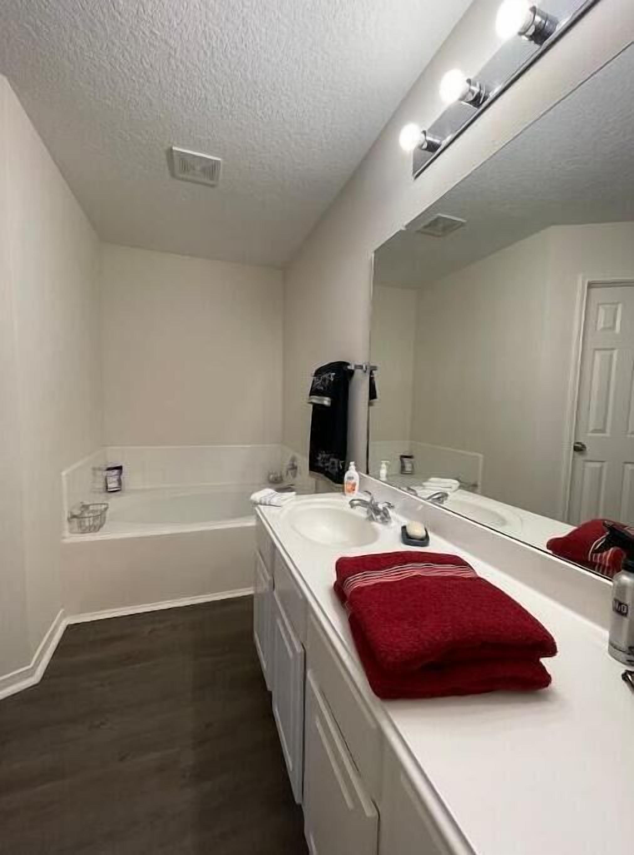 A bathroom with a white sink, a mirror, a red towel, and a shower.