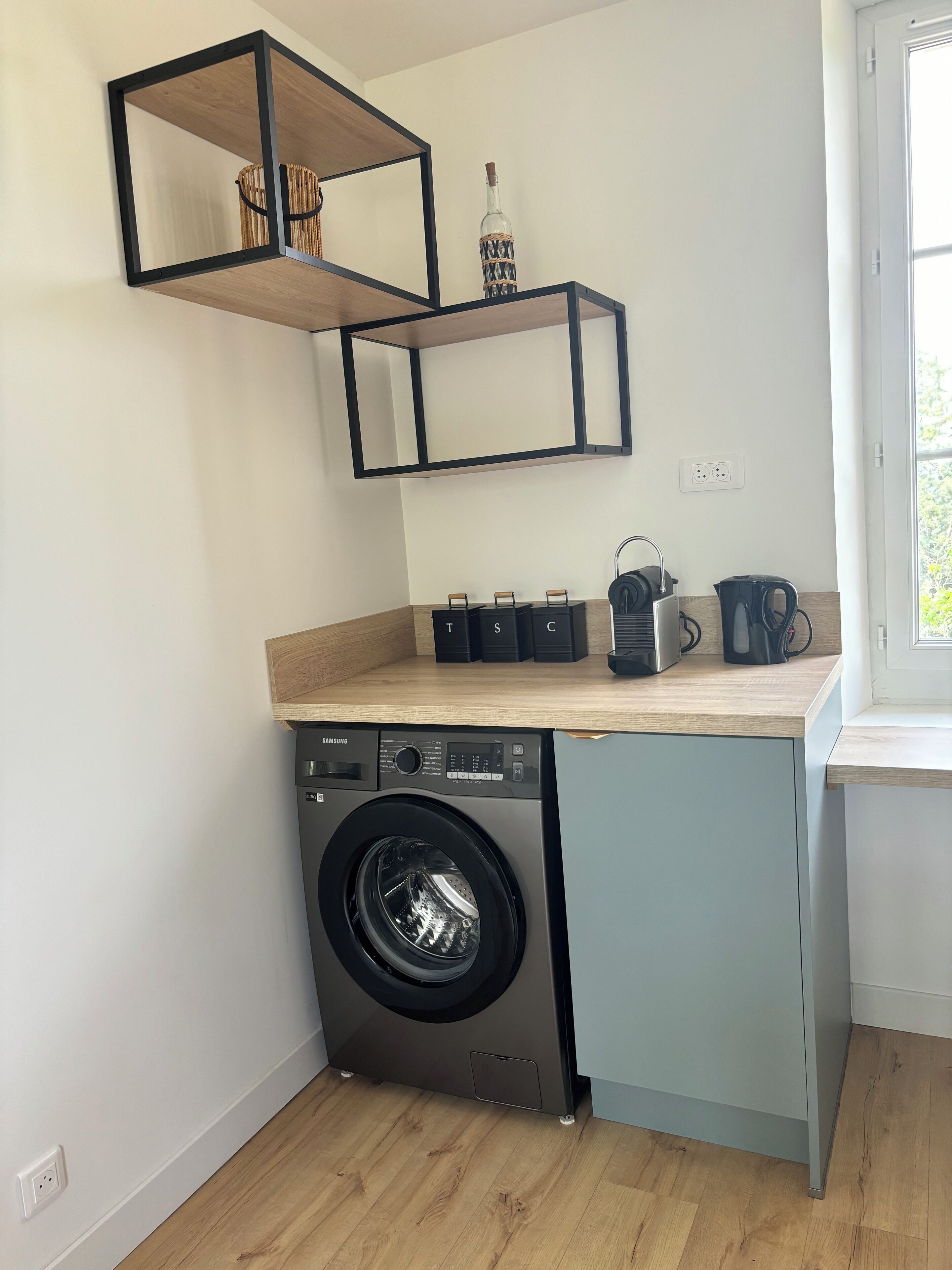 A compact kitchen with a built-in washer and dryer, wooden shelves, and a window.