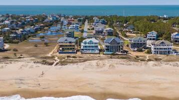 Una zona residencial costera con propiedades frente a la playa, incluyendo casas con amplios ventanales y balcones, una playa arenosa y el océano al fondo.