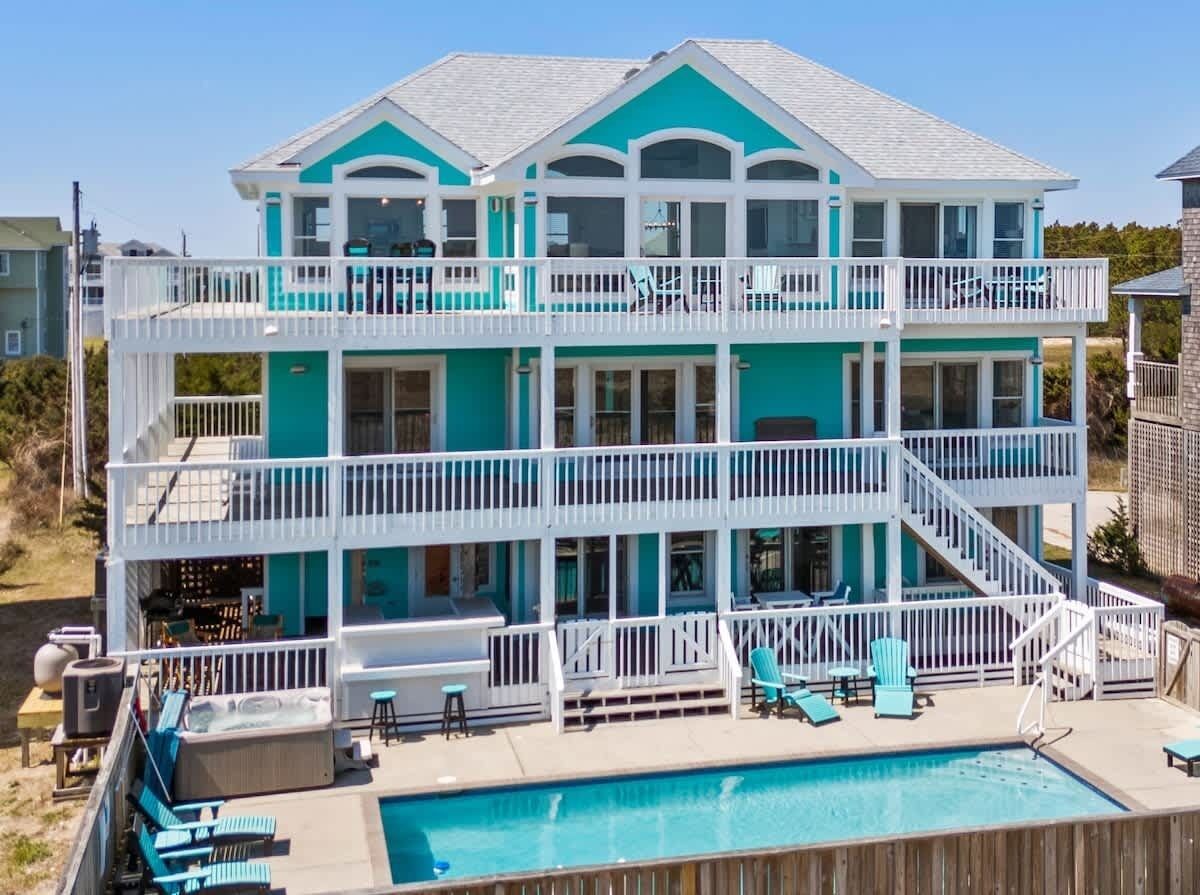 Une maison de deux étages située en bord de mer, dotée d’une piscine, de plusieurs balcons et d’espaces de détente extérieurs.