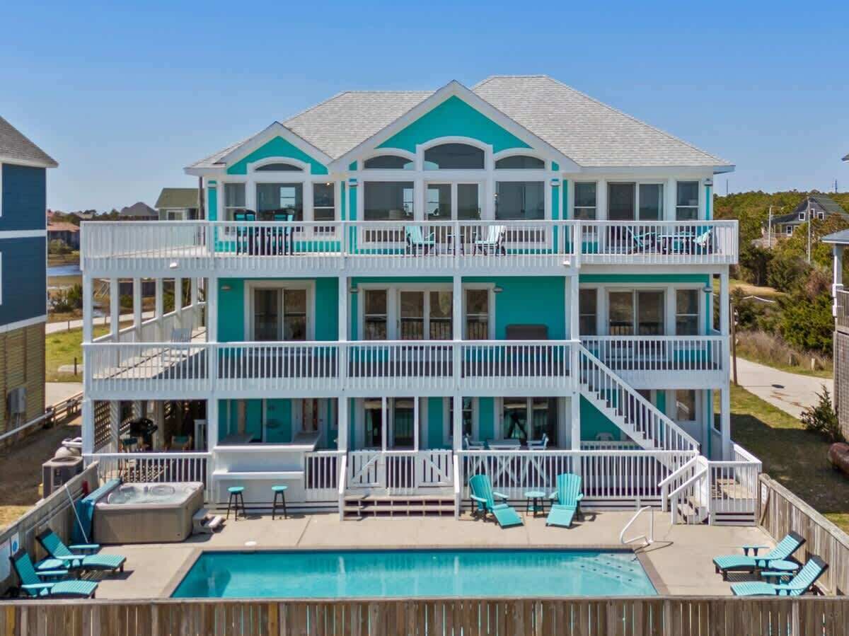 Casa frente al mar de dos pisos con piscina, varios balcones y mobiliario exterior.