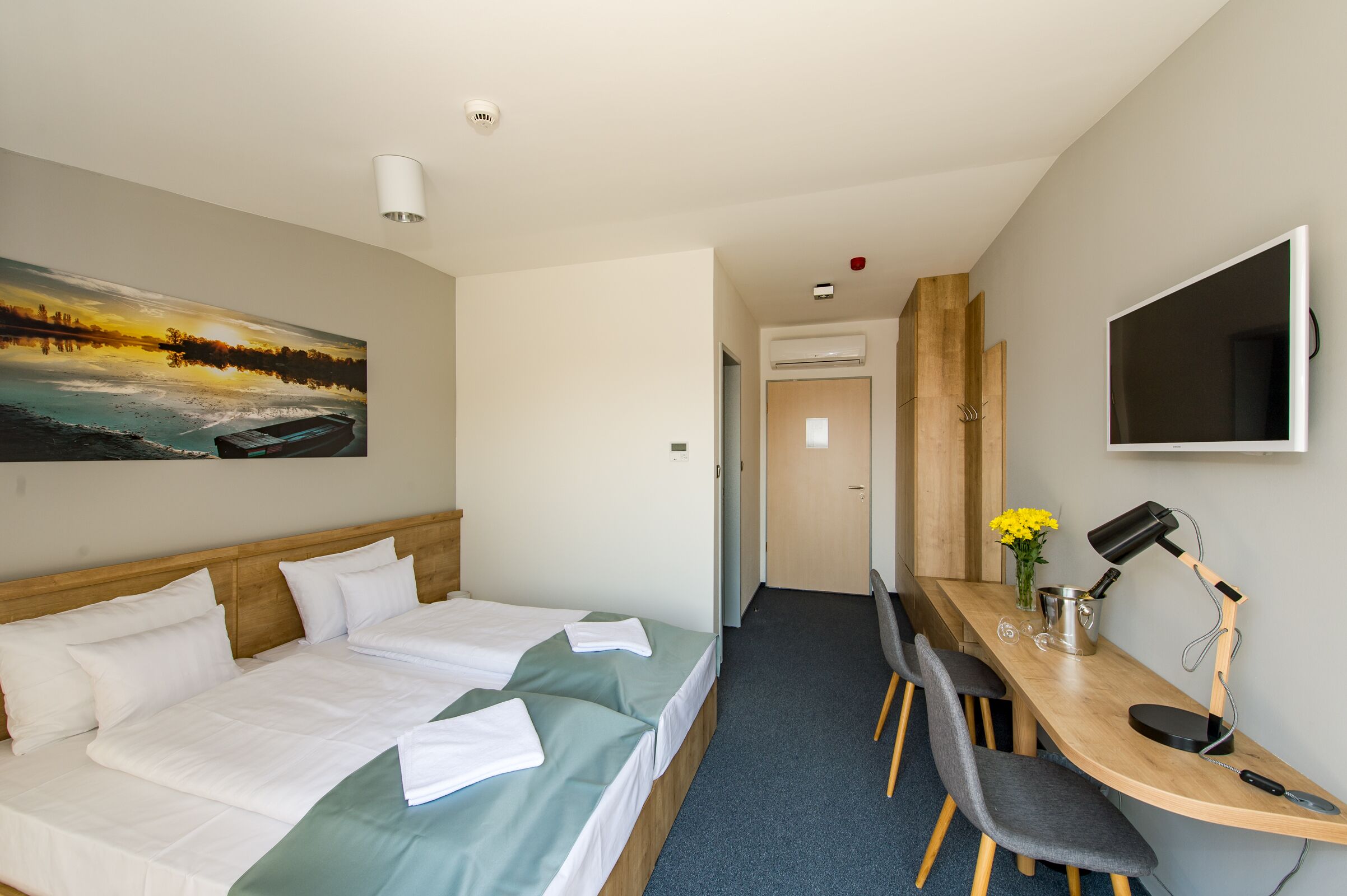 A hotel room with two beds, a desk with a chair, a TV, and a painting on the wall.