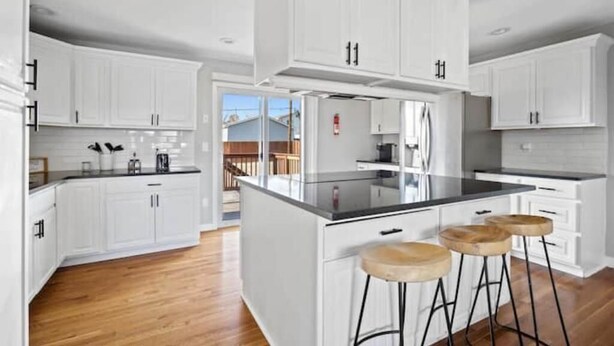 A modern kitchen with white cabinetry, a black countertop, and wooden stools. - Stylish Quiet Adobe - Elbert (Thornton)