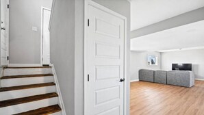 A staircase leading to a room with a white door, a grey couch, and a flat-screen TV. - Stylish Quiet Adobe - Elbert (Thornton)
