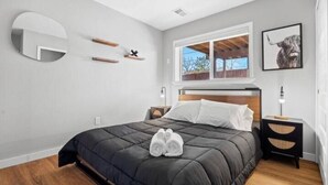 A modern bedroom with a large bed, a round mirror, and a window with a view of the outdoors. - Stylish Quiet Adobe - Elbert (Thornton)
