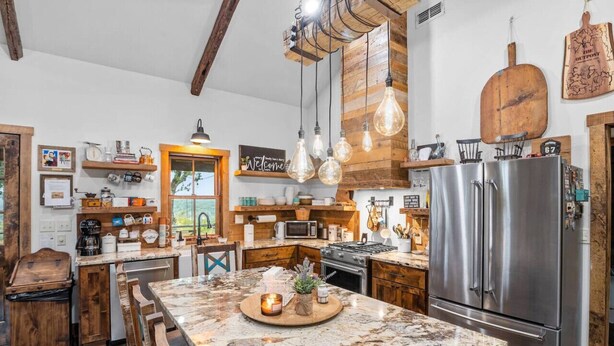 A rustic kitchen with a large island, wooden cabinets, and a stainless steel refrigerator. - The Outpost Vacation Cabin Fredericksburg TX Pet Friendly Hot Tub Near Enchanted Rock (Fredericksburg)