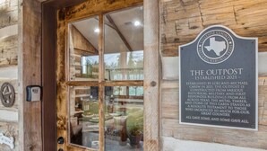 A wooden cabin entrance with a glass door and a plaque stating "THE OUTPOST - ESTABLISHED 2021 -". - The Outpost Vacation Cabin Fredericksburg TX Pet Friendly Hot Tub Near Enchanted Rock (Fredericksburg)