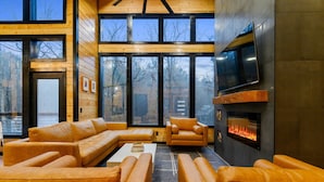 Una sala de estar moderna con sofás de cuero, chimenea y ventanas amplias con vistas al exterior.