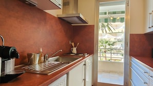 A modern kitchen with a stainless steel sink, a coffee machine, and a view of a balcony with palm trees. - 50 m² cocoon of Love with a common shared pool (Saint-Raphaël)