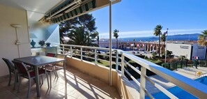 A balcony with a table and chairs, a pool, and a view of the sea and buildings. - 50 m² cocoon of Love with a common shared pool (Saint-Raphaël)