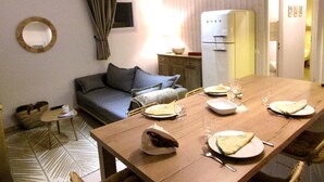 A dining area with a wooden table set for four, a sofa, a mirror, and a refrigerator in the background. - Beautiful 3 rooms with terrace near the ocean (Moliets-et-Maa)