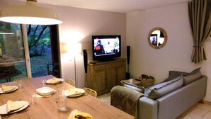 A dining area with a table set for two, a television on a wooden cabinet, and a grey sofa. - Beautiful 3 rooms with terrace near the ocean (Moliets-et-Maa)