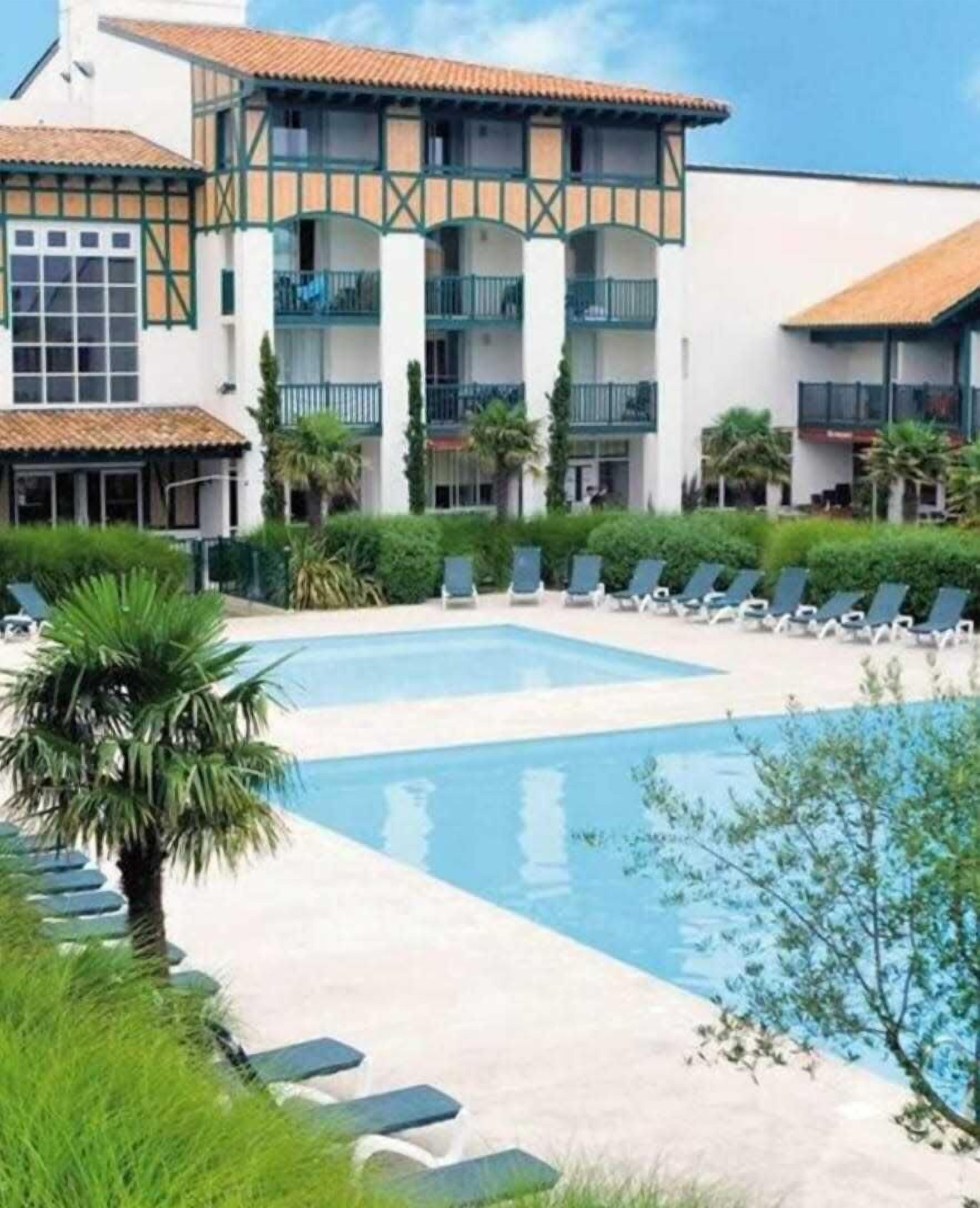 Ein Hotel mit Swimmingpool, Liegestühlen und Palmen.