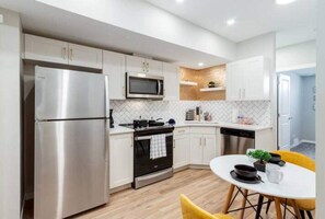 Una cocina moderna con electrodomésticos de acero inoxidable, armarios blancos y una silla de comedor amarilla.
