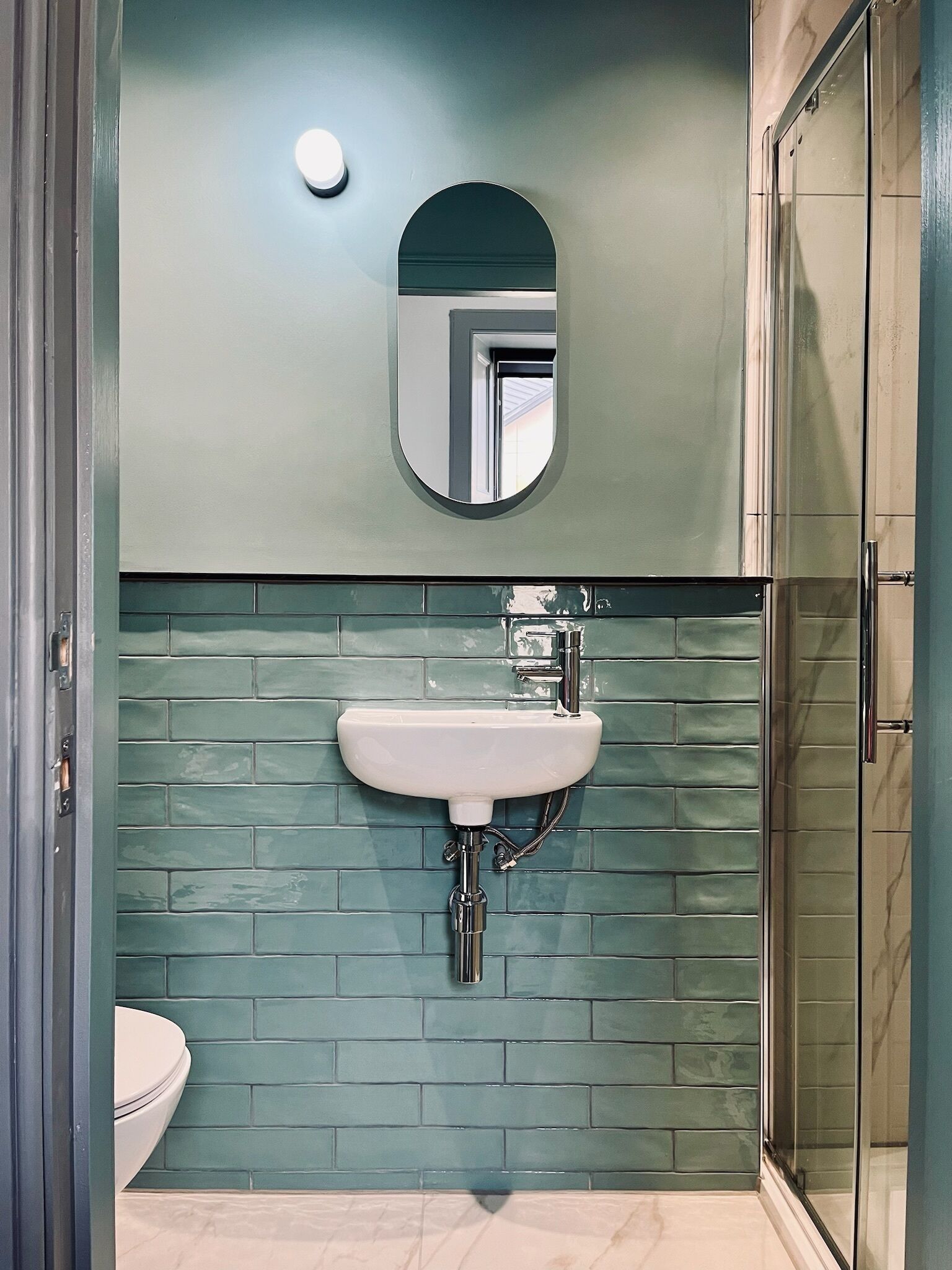 A bathroom with a white sink, a mirror above it, and a green-tiled wall.