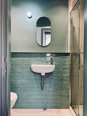 Une salle de bain avec un lavabo blanc, un miroir au-dessus et un mur recouvert de carreaux verts.