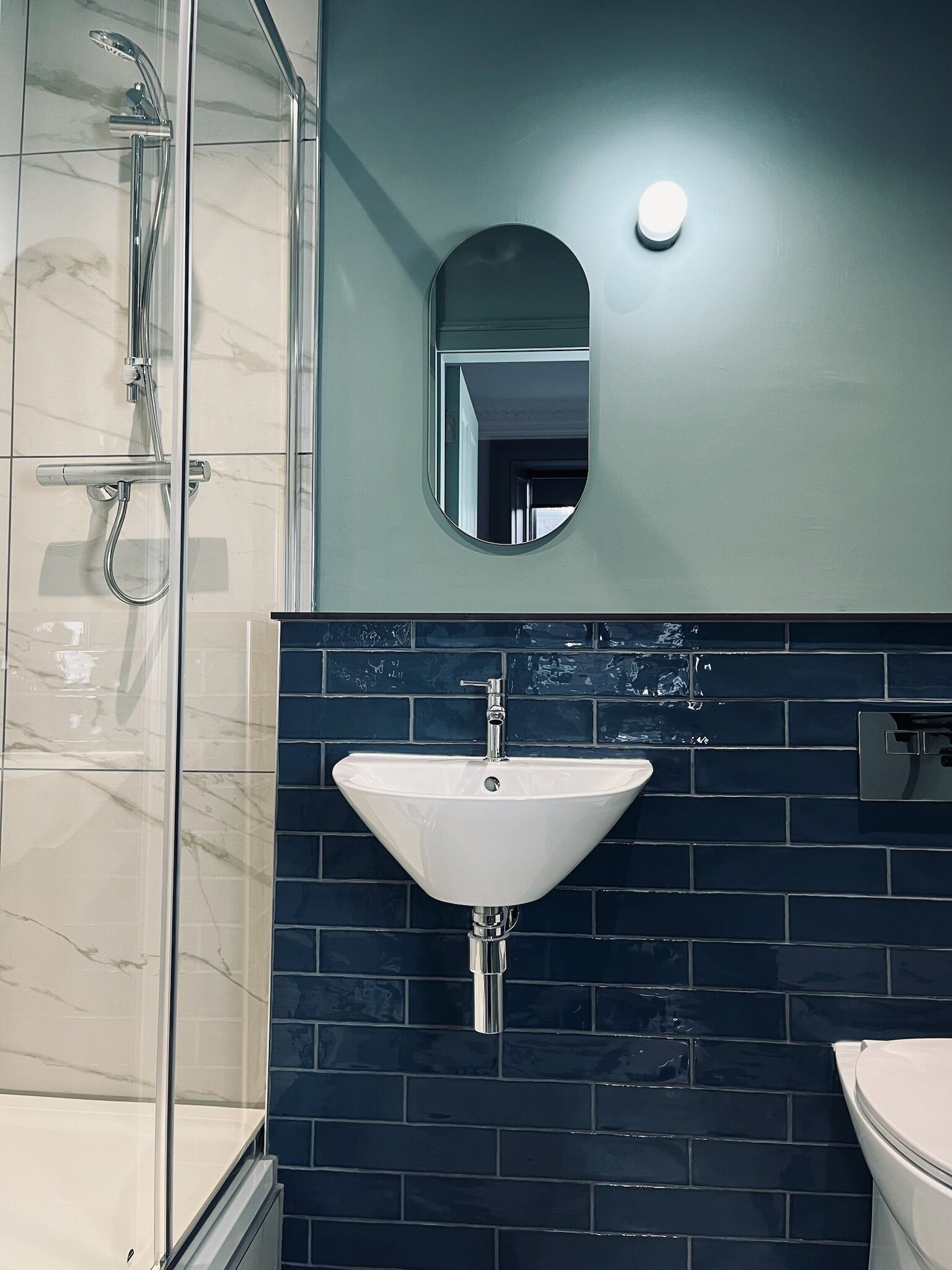 Un baño con cabina de ducha de vidrio, un lavabo blanco y un salpicadero de azulejos oscuros.