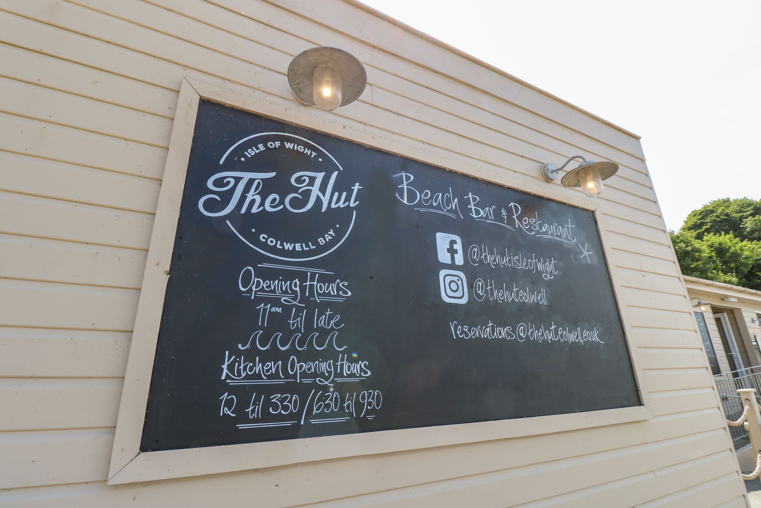 A chalkboard sign with the name 'The Hut' and details like opening hours and social media handles.