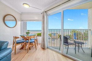 A balcony with a view of the sea, a dining area with a table and chairs, and a large mirror on the wall.