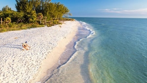 Una playa con aguas turquesas cristalinas, arena blanca y abundante vegetación verde.