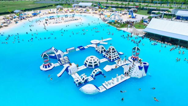 Vista aérea de un parque acuático con varias zonas de natación, toboganes y estructuras de juego.