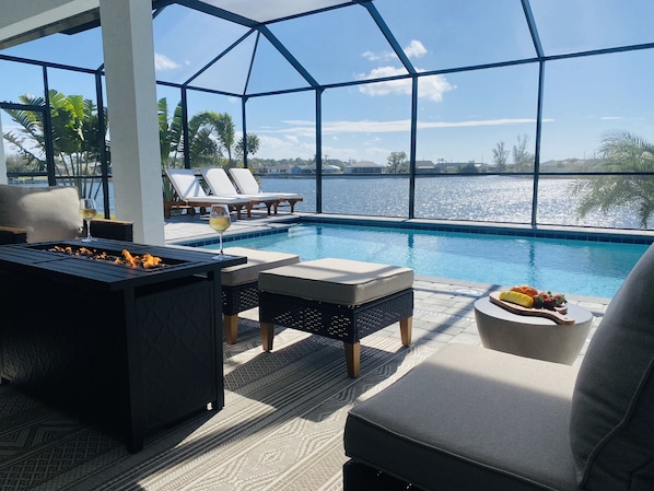 An indoor pool area with lounge chairs, a fire pit, and a table with a glass of wine.