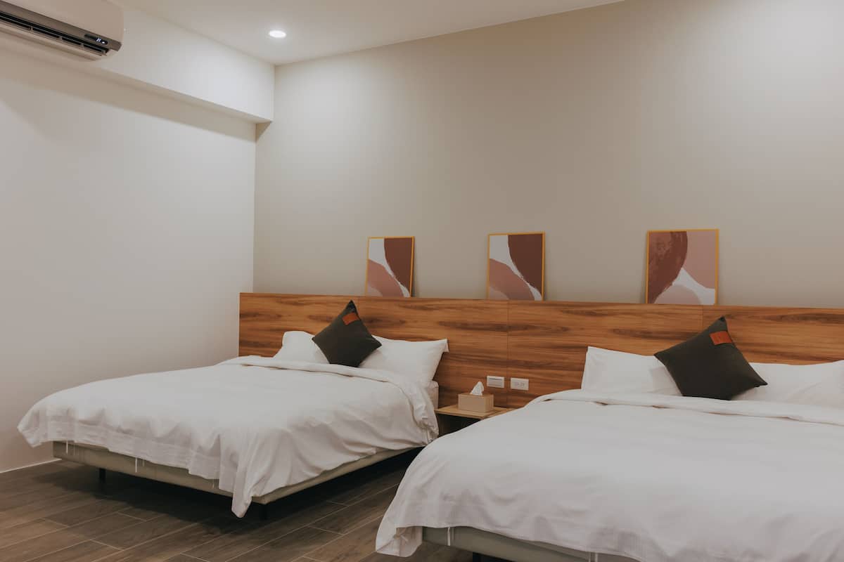A hotel room with two single beds, a wooden headboard, and a wall-mounted air conditioner.
