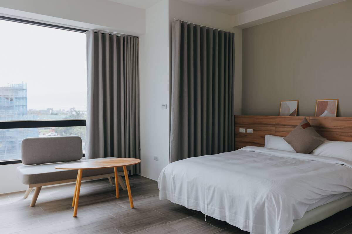 A modern hotel room with a large bed, a seating area, and a view of the city.