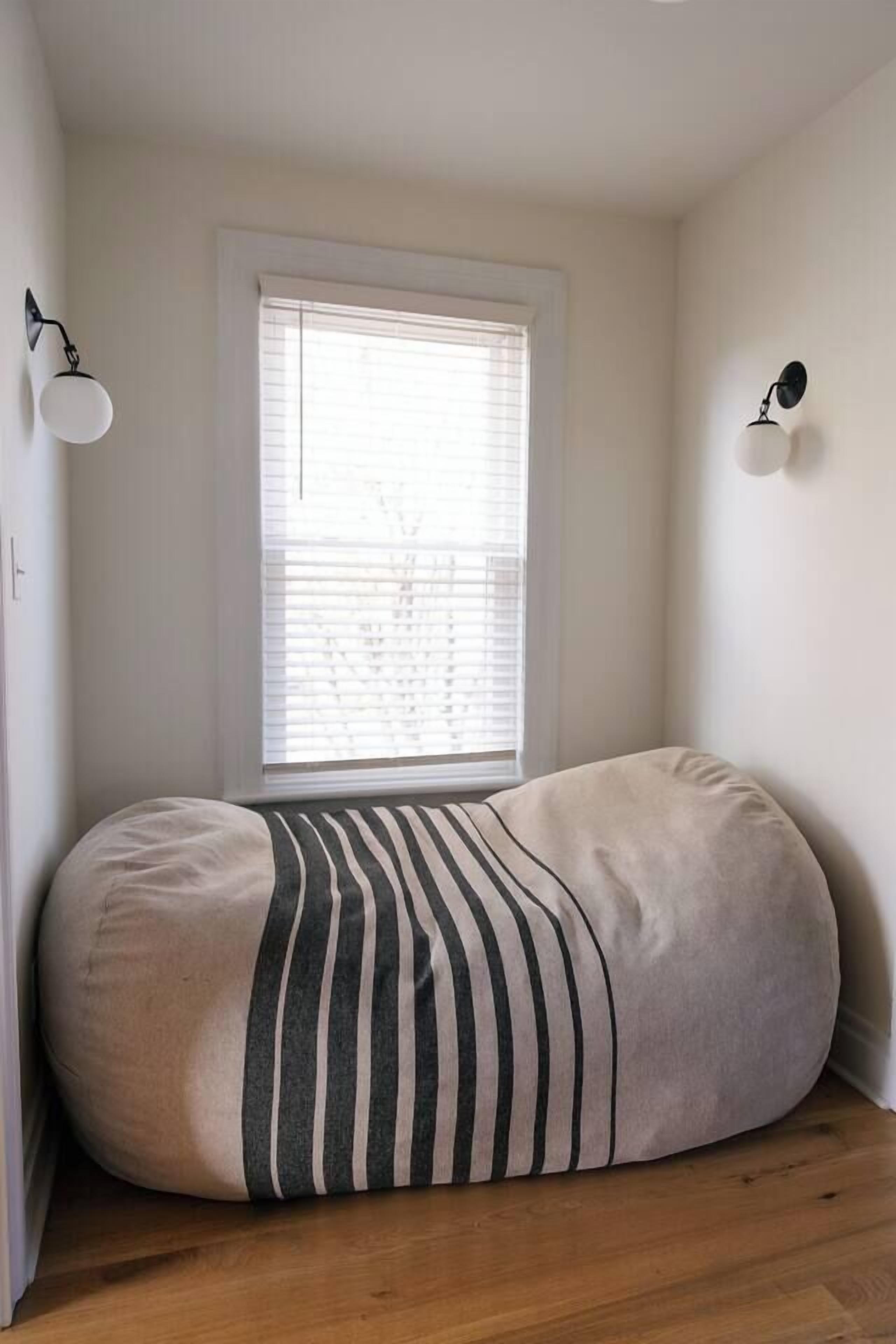 Une pièce avec un fauteuil en forme de poire, une fenêtre avec des stores et des lampes fixées au mur.
