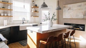 A modern kitchen with a central island, bar stools, pendant lighting, and a fireplace.