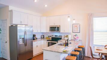 A modern kitchen with white cabinets, stainless steel appliances, a granite countertop, and a bar area with stools.