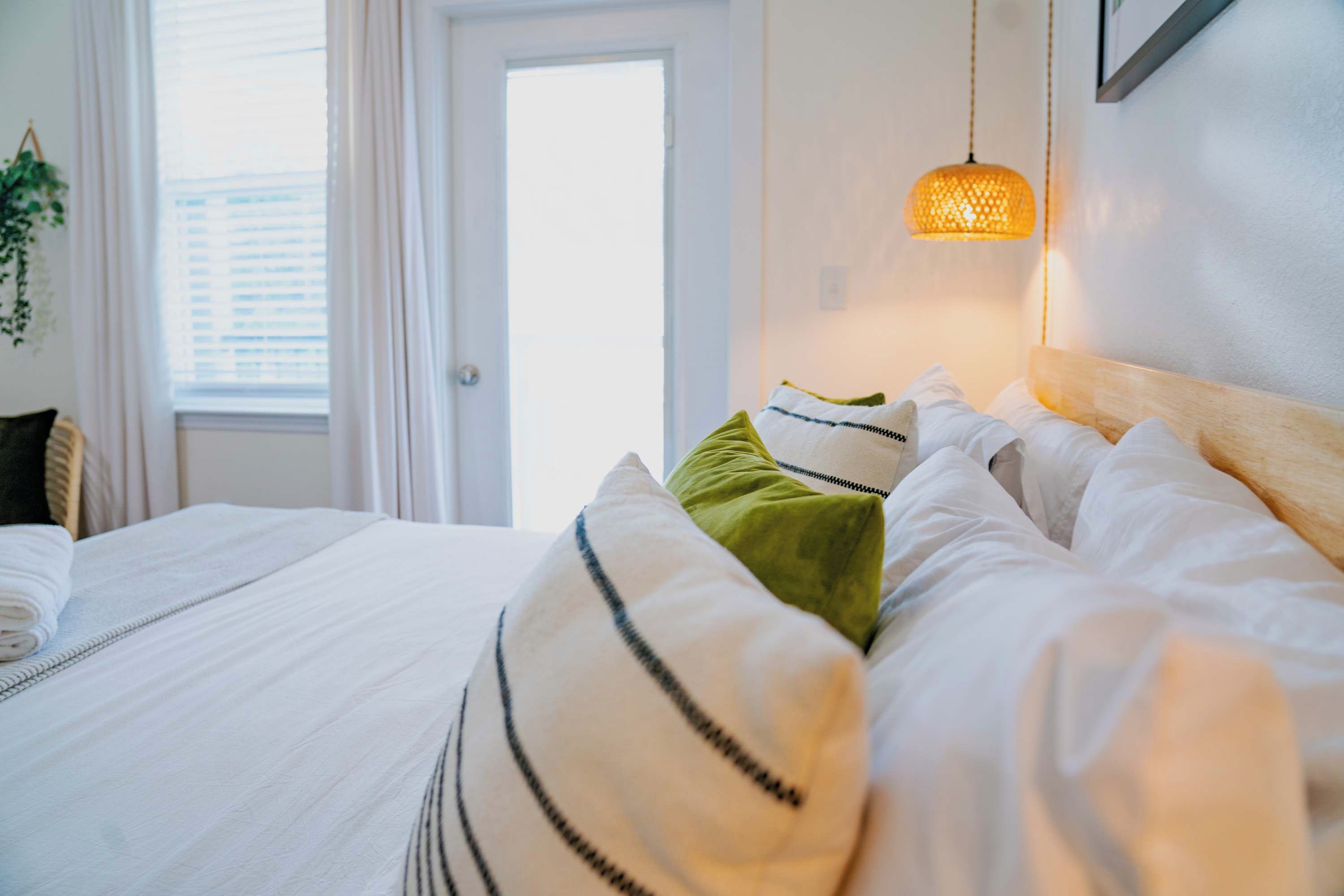Un lit bien fait, avec une literie blanche et des oreillers à rayures, un luminaire suspendu et une fenêtre avec des rideaux.