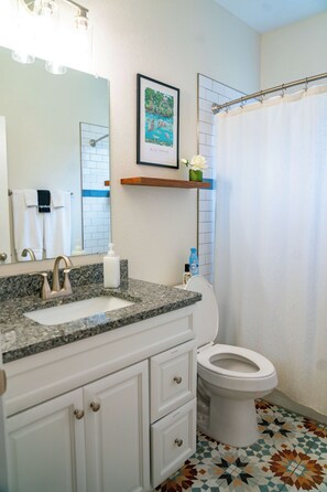 Une salle de bain avec un lavabo à dessus en granit, des toilettes blanches et un rideau de douche.