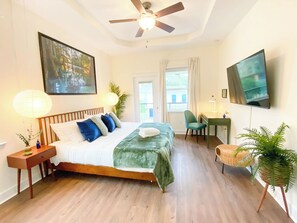 Une chambre à coucher comprenant un lit, des tables de chevet, un bureau, une chaise, un téléviseur et un ventilateur de plafond.