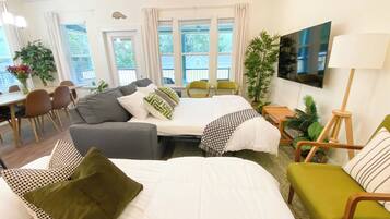 Ein modernes Hotelzimmer mit zwei Betten, einer Couch, einer Essecke und einem Fernseher.