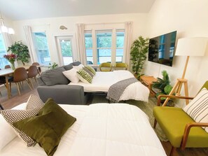 Moderni hotellihuone, jossa on kaksi sänkyä, sohva, ruokailutila ja televisio.