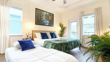 A hotel room with two beds, a ceiling fan, a large painting, and a view of the outdoors.