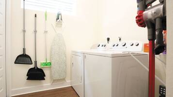 A laundry room with a washing machine, a dryer, and various cleaning tools.