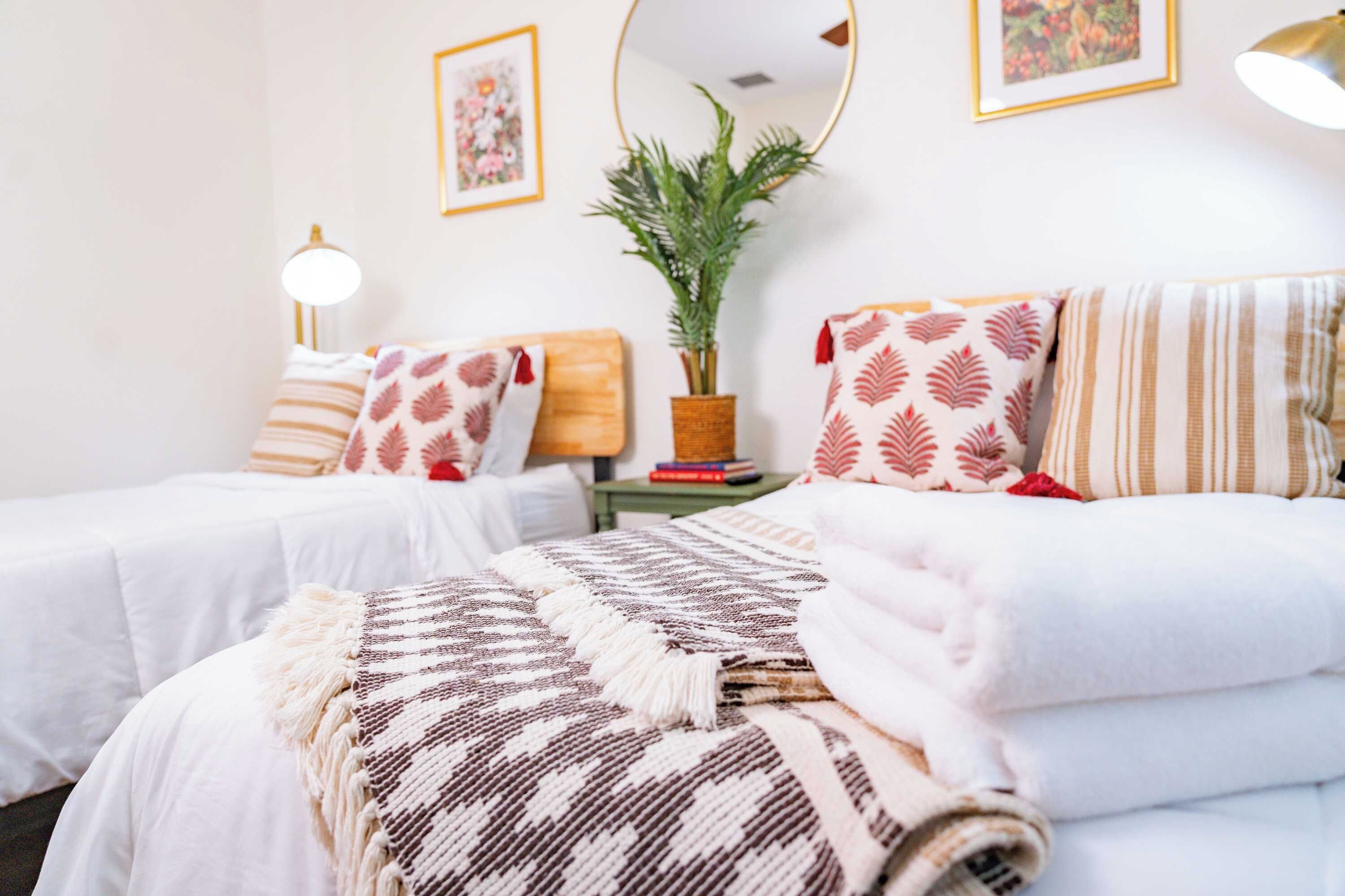 Une chambre d’hôtel avec deux lits, une plante en pot, des œuvres d’art encadrées et une lampe.