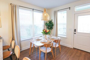 A dining area with a table set for four, surrounded by chairs, a hanging light fixture, and a potted plant.