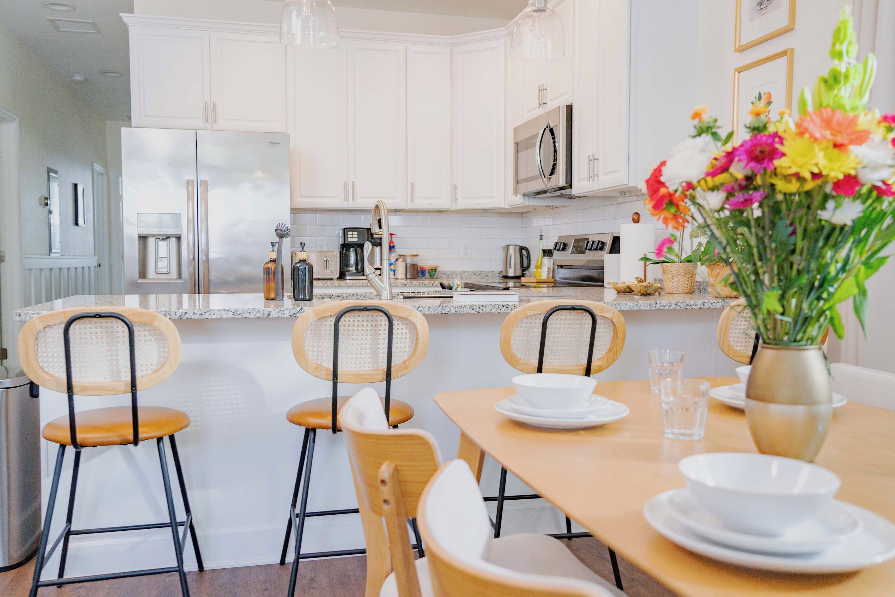 Une cuisine moderne avec des meubles blancs, des appareils en acier inoxydable et un coin repas comprenant des chaises en bois et une table dressée pour deux personnes.