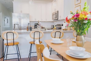 A modern kitchen with white cabinets, stainless steel appliances, and a dining area with wooden chairs and a table set for two.