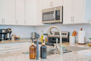 A kitchen with white cabinets, a stainless steel microwave, a coffee maker, and a sink with a modern faucet.