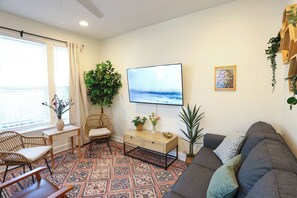 A living room with a sofa, a TV, a wooden side table, a patterned rug, and a large plant.
