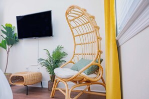 A room with a wicker chair, a television mounted on the wall, and potted plants.