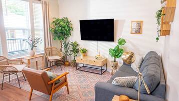 A living room with a sofa, chairs, a coffee table, a TV, and various plants.