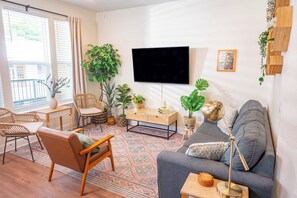 A living room with a sofa, chairs, a coffee table, a TV, and various plants.