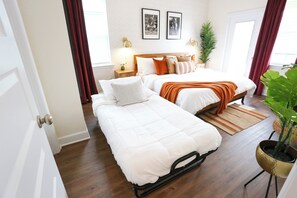 A bedroom with two beds, a wooden headboard, a nightstand, a lamp, and a potted plant.