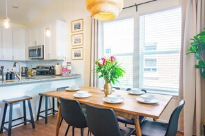 A modern kitchen with white cabinets, a microwave, and a dining area with a wooden table and black chairs.